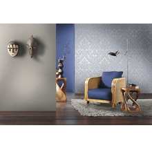 Wohnzimmer mit floral gemusterter Tapete, Sessel und dekorativen Holzmasken