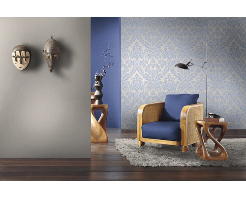 Wohnzimmer mit floral gemusterter Tapete, Sessel und dekorativen Holzmasken