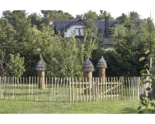 Trois ruches en bois derrière une clôture en bois dans un jardin.