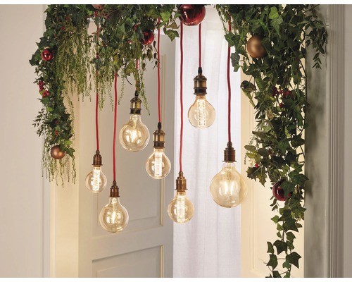 Dekorative Glühbirnen hängen von einer Girlande mit Pflanzen und Weihnachtskugeln
