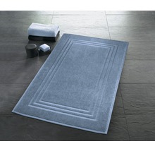 Rechteckige Badematte mit umlaufendem Rahmenmuster, daneben liegen Handtücher und Badutensilien