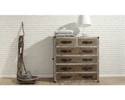 Commode en bois avec six tiroirs, décoration et lampe devant un mur de briques