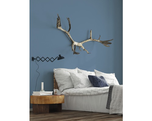 Chambre avec lit, table de chevet, lampe et bois de cerf au mur.