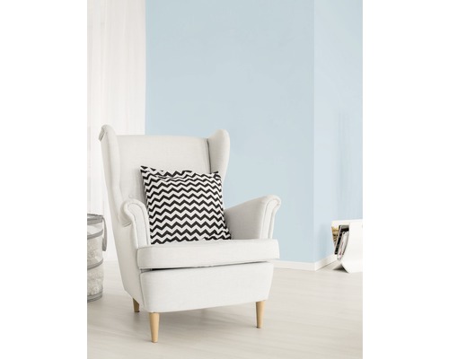 Salon lumineux avec peinture murale bleu pastel, fauteuil blanc et coussin à motif zigzag