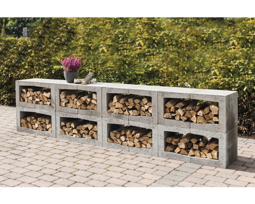 Holzlager aus Betonsteinen mit Holzscheiten und einer Pflanze im Topf