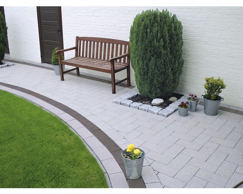 Chemin de jardin avec pavés, banc en bois et pots de fleurs.