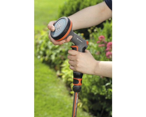 Une personne tient une lance d''arrosage Gardena dans la main, reliée à un tuyau d''arrosage.