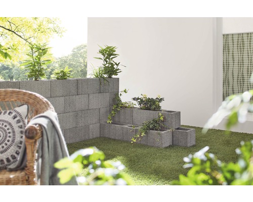 Des blocs de béton empilés forment un mur de jardin et des bacs à fleurs avec des plantes