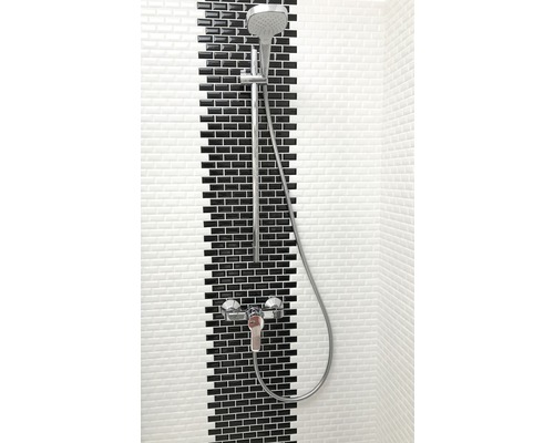 Robinet de douche avec douchette à main devant un mur avec des carreaux noirs et blancs