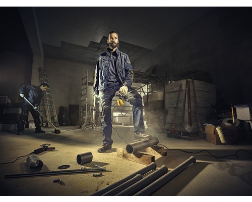 Artisan en vêtements de travail avec perceuse dans un entrepôt avec des tuyaux et des outils.