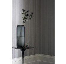 Vase décorative en verre avec fleur sur une table d''appoint devant un papier peint rayé.