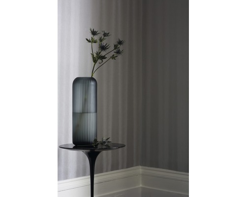 Vase décorative en verre avec fleur sur une table d''appoint devant un papier peint rayé.