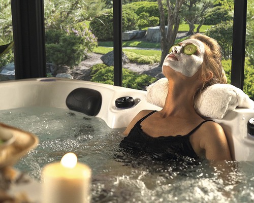 Une femme se détend avec un masque facial et des tranches de concombre dans un bain à remous dans le jardin.