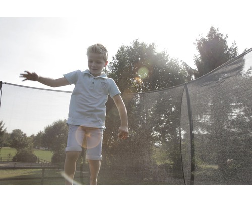 Junge springt auf Gartentrampolin mit Sicherheitsnetz