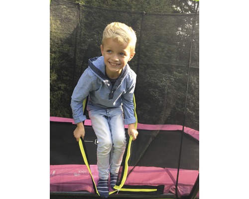Garçon grimpant sur un trampoline de jardin avec filet de sécurité