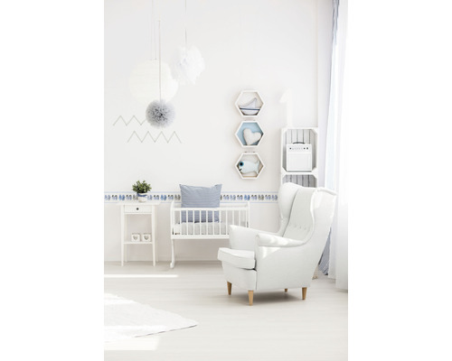 Helles Kinderzimmer mit Kinderbett, Sessel, Beistelltisch und Wanddekoration