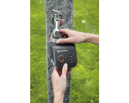 Une personne fixe un programmateur d''arrosage Gardena Smart Water Control sur un robinet extérieur.