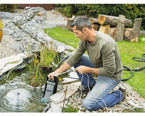 Un homme utilise une pompe de bassin dans un bassin de jardin avec jet d''eau.