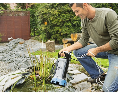 Un homme utilise une pompe de bassin sur le bassin de jardin.