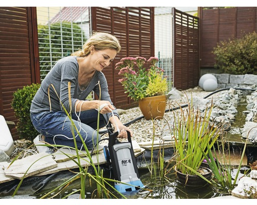 Femme actionnant une pompe de bassin de la marque for_q dans un bassin de jardin.