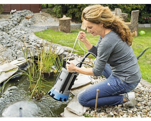 Une femme laisse tomber une pompe submersible dans un bassin de jardin