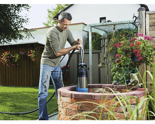 Un homme actionne une pompe à levier manuelle au puits dans le jardin.