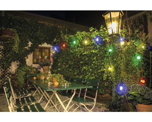 Extérieur avec mobilier de jardin vert, éclairé par une guirlande lumineuse et une lanterne.