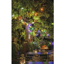 Jardin illuminé avec tables, chaises et lanternes sous un arbre avec des guirlandes lumineuses.