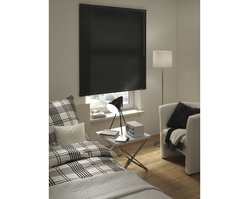 Schlafzimmer mit Fenster und schwarzem Rollo, Bett, Sessel und Lampe