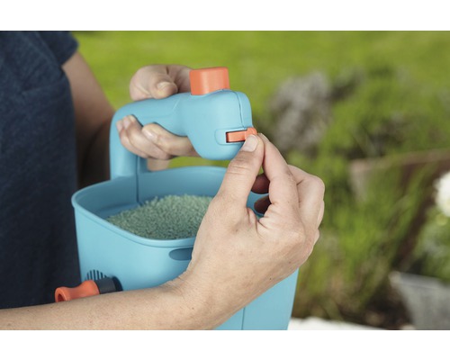 Person betätigt Dosierhebel an einem Handstreuer gefüllt mit Rasensamen.