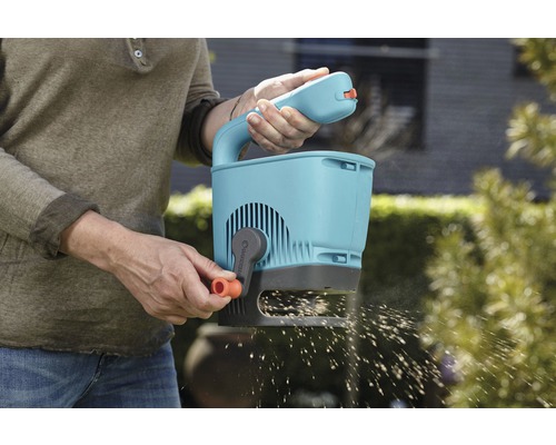 Eine Person benutzt einen Gardena Streuwagen im Garten, um Saatgut auszubringen.