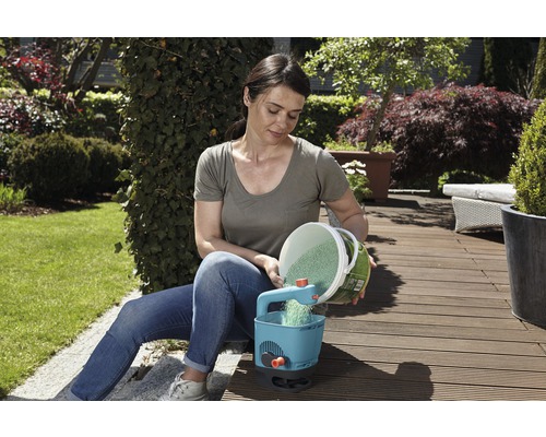 Eine Frau befüllt einen Düngerstreuer mit Dünger in einem Garten.