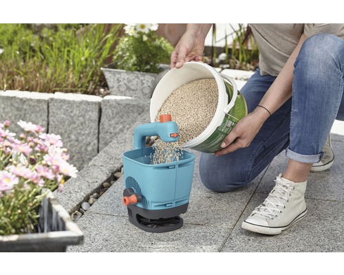 Person füllt Dünger in einen Streuwagen im Garten.