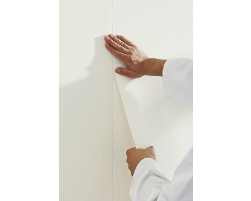 Eine Person bringt eine Tapete an einer Wand an