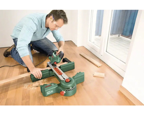 Un homme agenouillé coupe du bois à la scie sauteuse avec une boîte à onglets