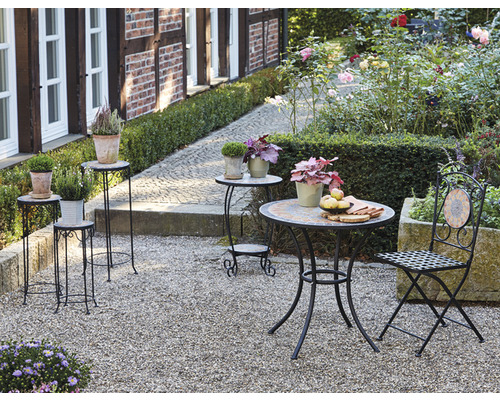 Gartenszene mit Pflanzensäulen, Tisch und Stuhl auf Kiesweg.