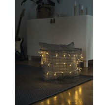 Scène décorative avec un panier rempli d'une guirlande lumineuse et d'un coussin sur un tapis