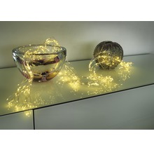 Guirlande lumineuse décorative drapée autour d'un saladier en verre et d'un vase sphérique sur un meuble.