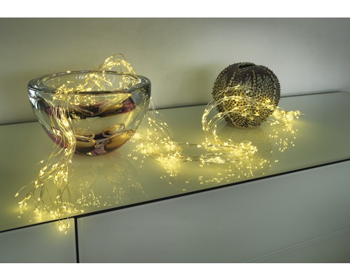 Guirlande lumineuse décorative drapée autour d'un saladier en verre et d'un vase sphérique sur un meuble.