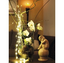 Vase décorative en verre avec fleurs d'orchidées, branches et guirlande lumineuse à côté d'une statue d'ange
