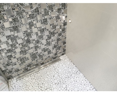 Salle de bains avec mur en mosaïque, carrelage au sol imitation galets et caniveau d''écoulement