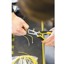 Une personne utilise une pince à dénuder sur un câble jaune.