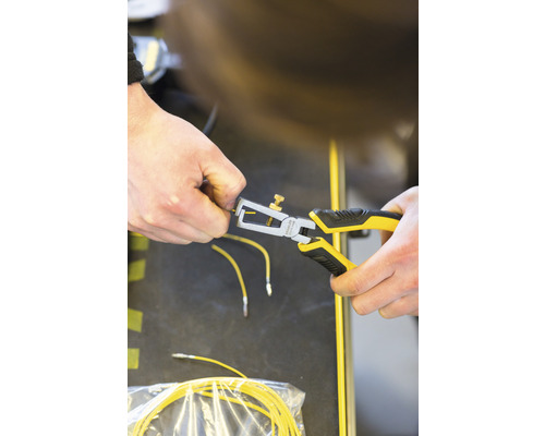 Une personne utilise une pince à dénuder sur un câble jaune.