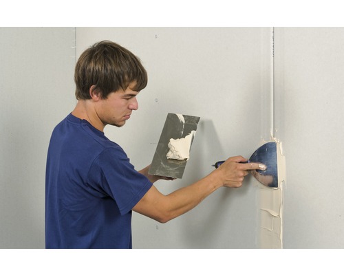 Mann spachtelt eine Wand mit Spachtelmasse und einem Spachtel