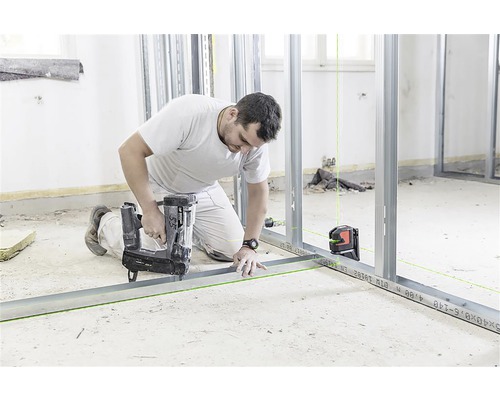 Mann befestigt Metallständerwerk mit einem Bolzensetzer und einem Laser