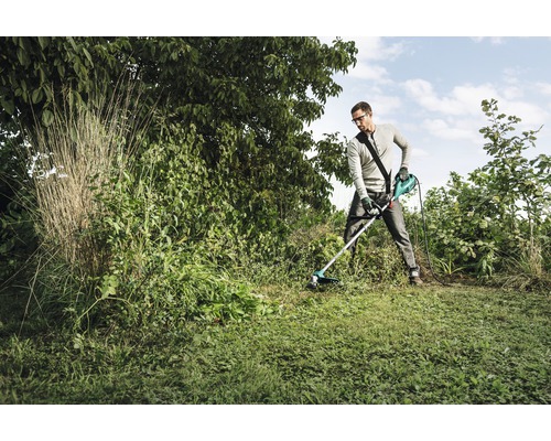 Mann arbeitet mit einem Rasentrimmer im Garten.