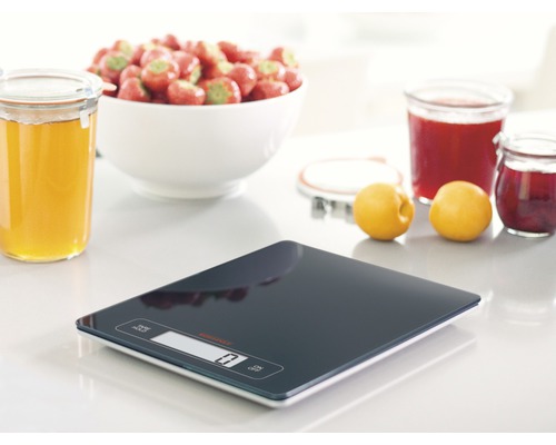 Digitale Küchenwaage mit Schüssel Erdbeeren, Quitten, Marmelade und Honig auf einem Tisch.