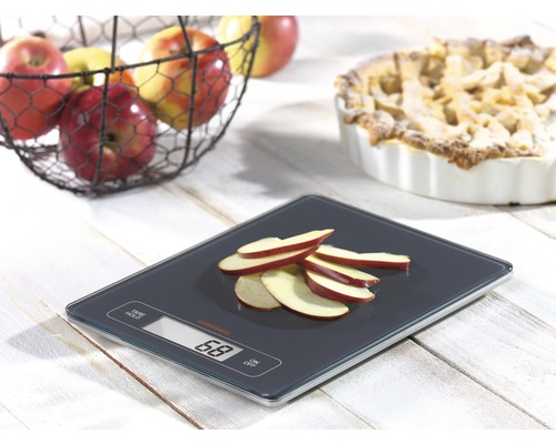 Digitale Küchenwaage mit Apfelscheiben, Korb mit Äpfeln und Apfelkuchen