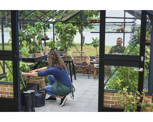 Gewächshaus mit Pflanzen, Gartengeräten und zwei Personen
