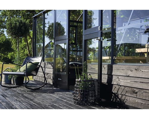 Aussenansicht eines Gewächshauses mit Glaswänden, einer Sitzgelegenheit und dekorativen Pflanzen auf einer Holzterrasse